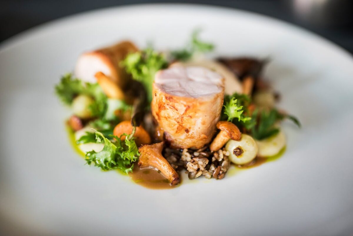 Close-up of a gourmet chicken dish with wild rice, mushrooms, and greens on a white plate.
